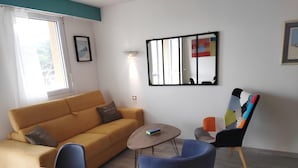 A living room with a sofa, a coffee table, a chair, and a mirror on the wall. - Studio Apartment 'Au Coeur De Quiberon' with Shared Pool, Balcony and Wi-Fi (Quiberon)