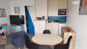 A modern living room with a TV, sofa, and dining area with chairs and a table. - Studio Apartment 'Au Coeur De Quiberon' with Shared Pool, Balcony and Wi-Fi (Quiberon)