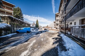 Eine verschneite Straße mit Gebäuden an beiden Seiten, ein blauer Van ist links geparkt, und ein klarer, blauer Himmel.