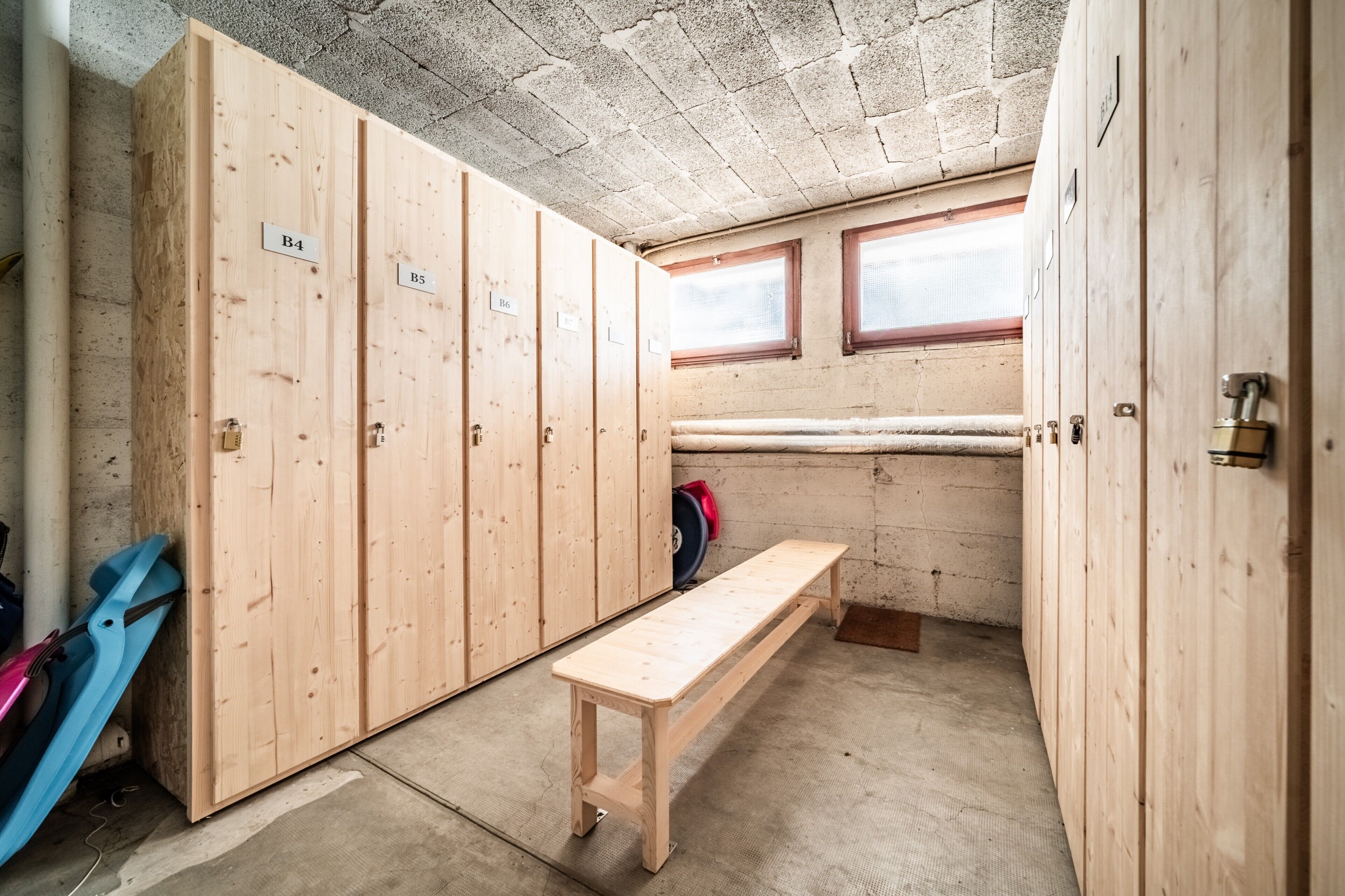 Un vestiaire avec des casiers en bois portant les numéros B3, B4 et B6, un banc et une fenêtre.