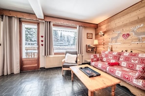 Ein gemütliches Zimmer mit einer Holzbank, einem roten, gemusterten Sofa, einem Holzrahmenfenster und einer Wandlampe.