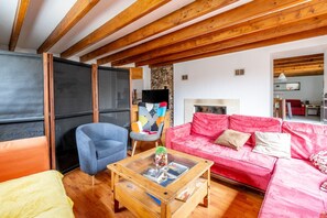 A living room with a red sofa, a blue armchair, a wooden coffee table with magazines, and a stone wall.