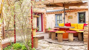 Une terrasse avec des tables et des bancs en bois, un espace de repos couvert et un chemin en pierre.