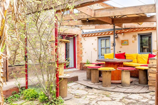 A patio with wooden tables and benches, a covered seating area, and a stone pathway.