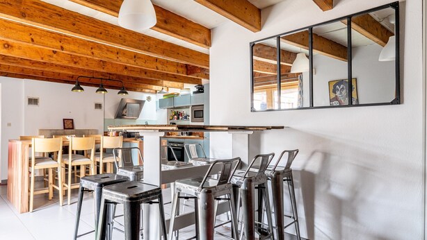 Une cuisine moderne avec des poutres en bois, un coin bar avec des tabourets et un grand miroir au mur.