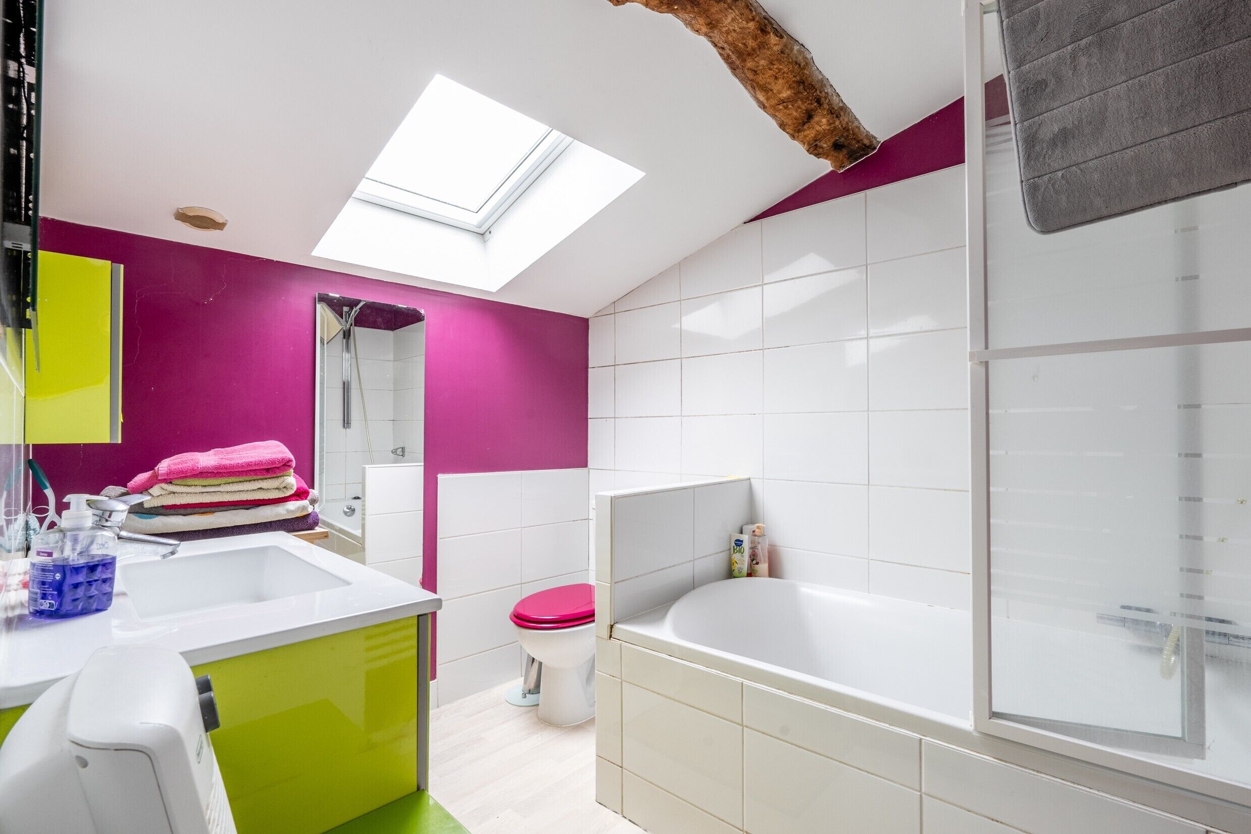 A modern bathroom with a skylight, a bathtub, a sink, and a toilet.
