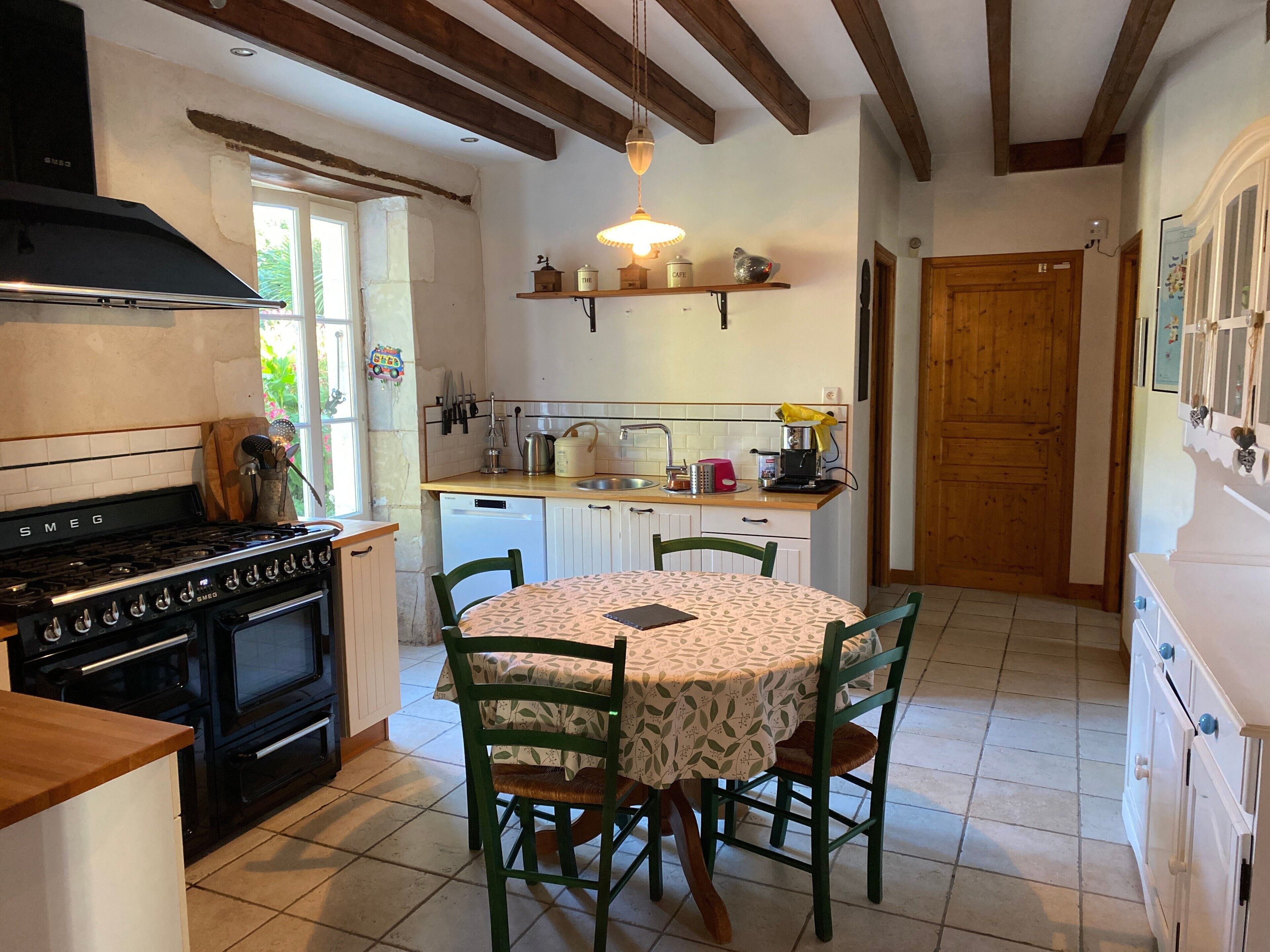 Une cuisine équipée d’une cuisinière, d’un four et d’un évier, avec des poutres en bois, une table à manger et des chaises, ainsi qu’un réfrigérateur.