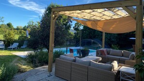 A covered outdoor seating area with wicker furniture, a pool, and a pergola structure.
