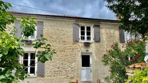 A stone building with a gravel driveway, a small door, and windows with shutters.