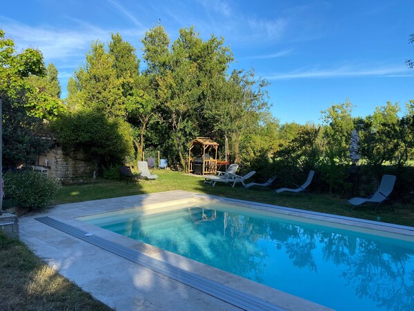 A swimming pool with lounge chairs, a wooden gazebo, and surrounding greenery.