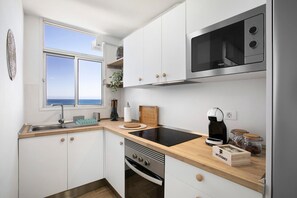 Una cocina compacta con ventana, microondas, cafetera y una caja etiquetada 'INFUSIONES'.