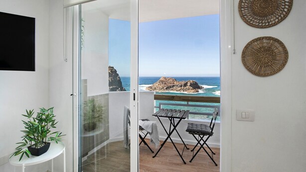 Een balkon met uitzicht op zee, een bloempot en twee geweven wanddecoraties.