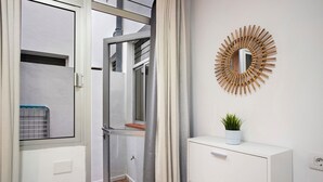 Een moderne badkamer met een glazen douchedeur, een witte kast met lades en een zonvormige spiegel aan de muur.