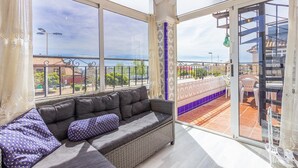 A balcony with a wicker sofa, a view of the cityscape, and a tiled floor.