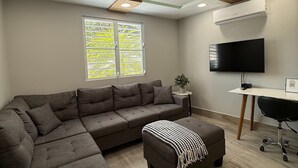 Un salon moderne avec un canapé d’angle, un téléviseur à écran plat et un plafond agrémenté de luminaires aux formes géométriques.