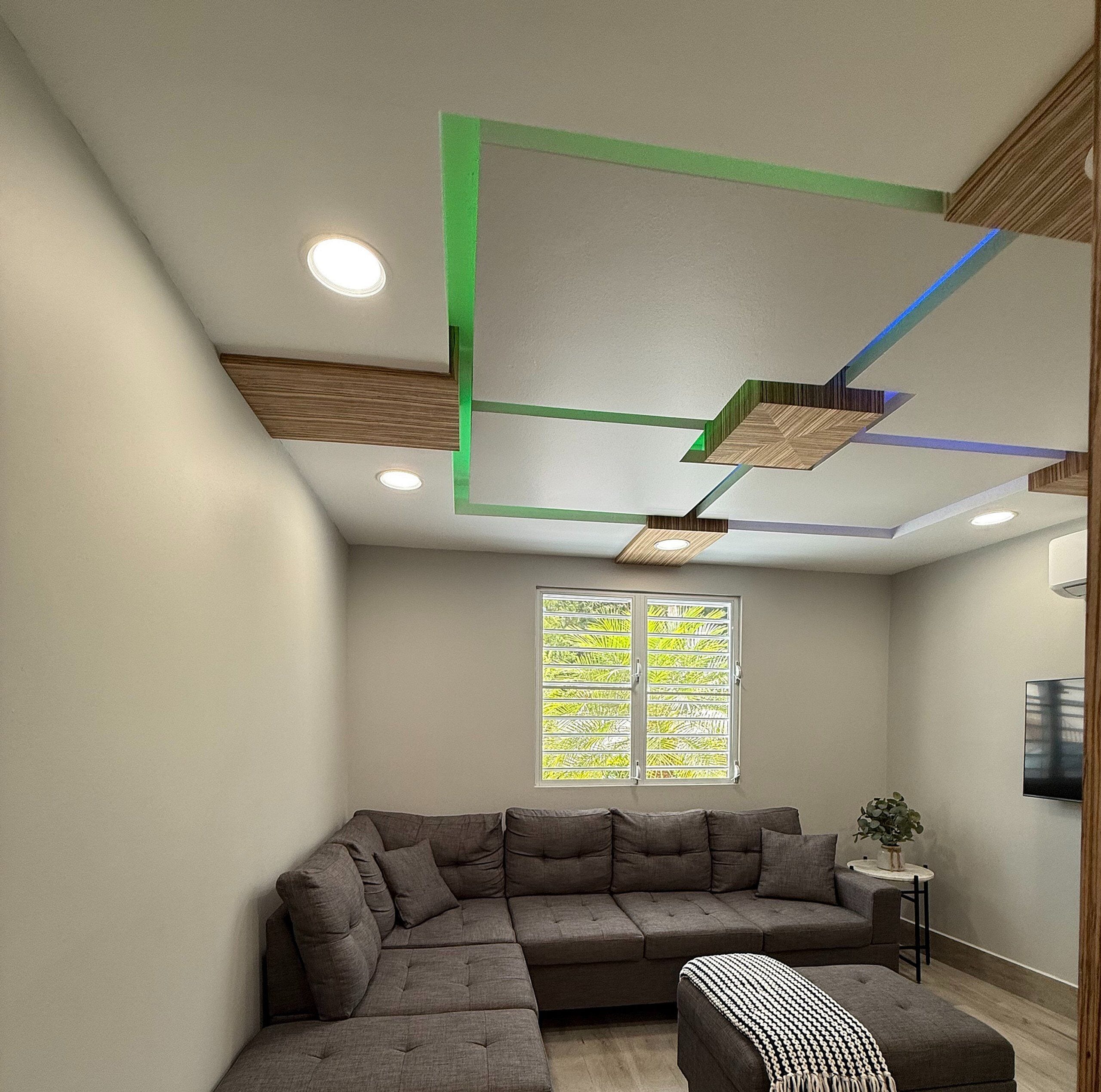 Un salon moderne avec un canapé d’angle, une petite table d’appoint et un téléviseur fixé au mur.