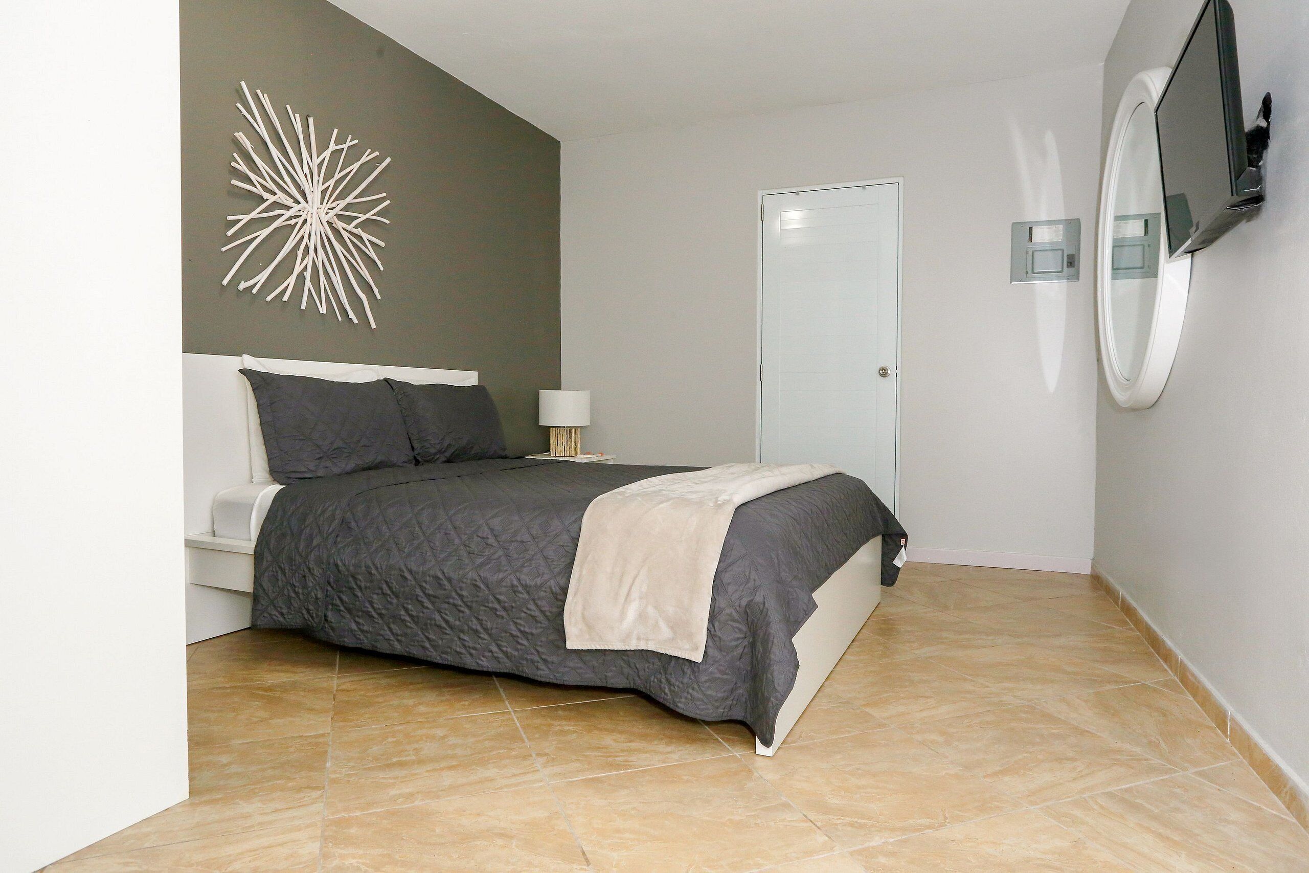 A bedroom with a bed, a wall-mounted TV, a door, and a decorative wall piece.