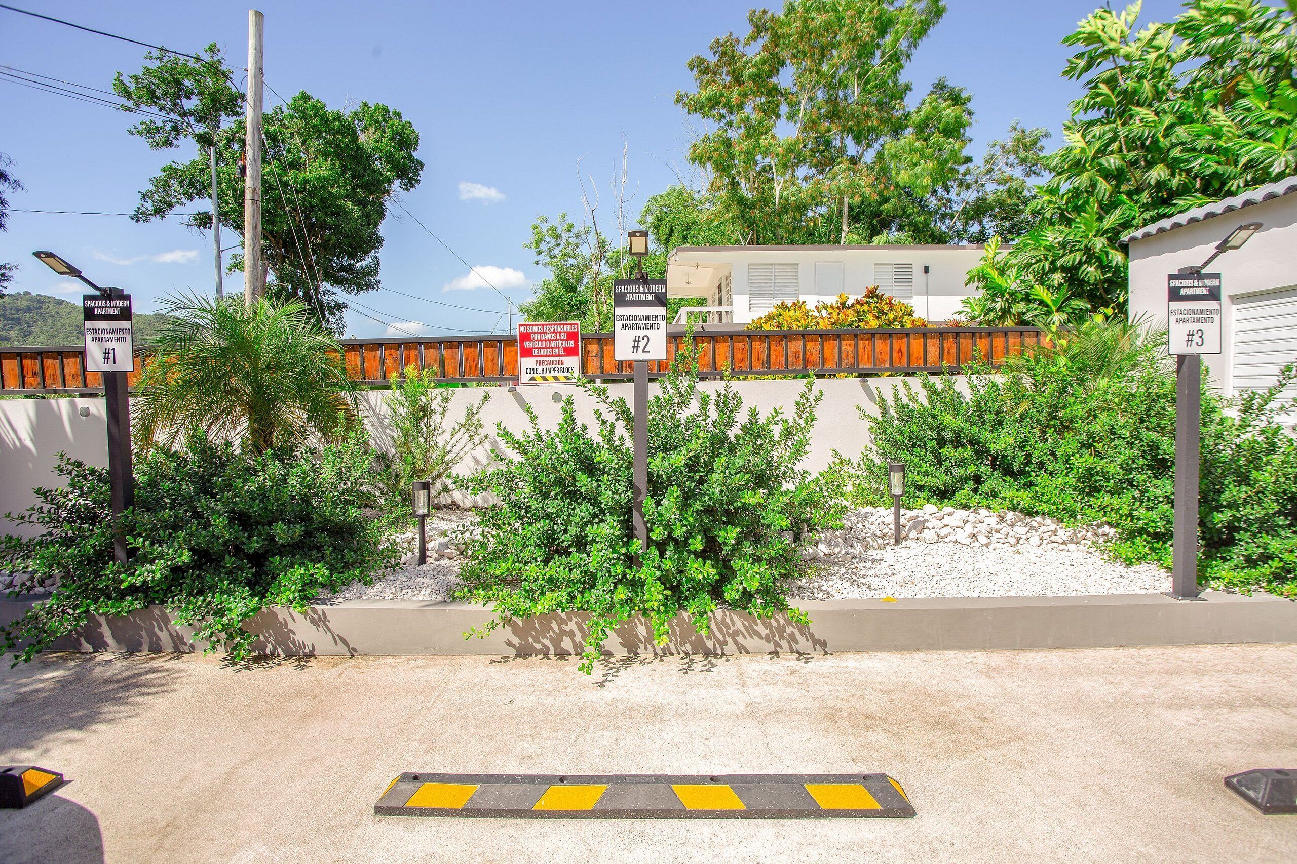 A gated residential area with multiple apartment signs, a concrete pathway, and surrounding greenery.