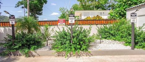A gated residential area with multiple apartment signs, a concrete pathway, and surrounding greenery.