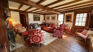 Una sala de estar acogedora con pisos de madera, sillones con estampado rojo y blanco, un sofá rojo y techo de madera con vigas a la vista.