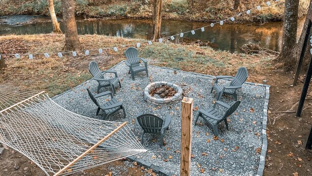 An outdoor seating area with Adirondack chairs and a fire pit, surrounded by a wooden deck and a rope fence. - Nature's Cedar Creek Getaway-K
 (Cave Spring)