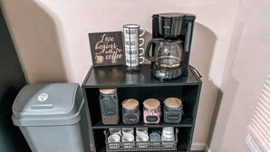 A coffee station with a coffee maker, a sign saying "Love begins with coffee," and jars labeled "Coffee," "Creamer," "Sugar," and "Hollandaise." - Nature's Cedar Creek Getaway-K
 (Cave Spring)