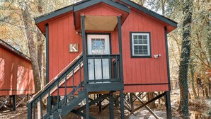 A red wooden cabin with a small porch and a staircase leading to the entrance. - Nature's Cedar Creek Getaway-K
 (Cave Spring)