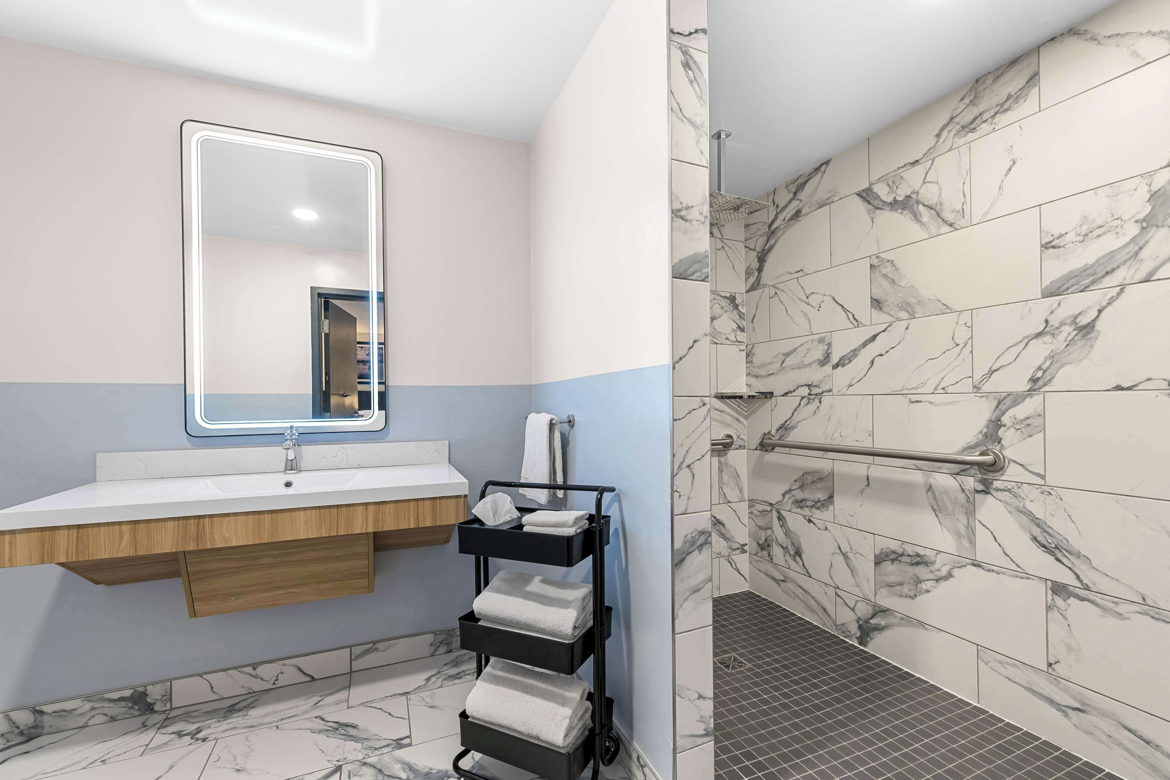 A bathroom with a marble-tiled shower, a vanity with a mirror, and a towel rack.