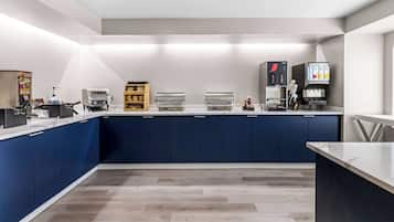A modern kitchen with blue cabinets, a marble countertop, and various appliances including a coffee machine and a food warmer.