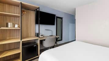 Una habitación de hotel con una cama, un escritorio con silla, televisión, armario y un refrigerador pequeño.