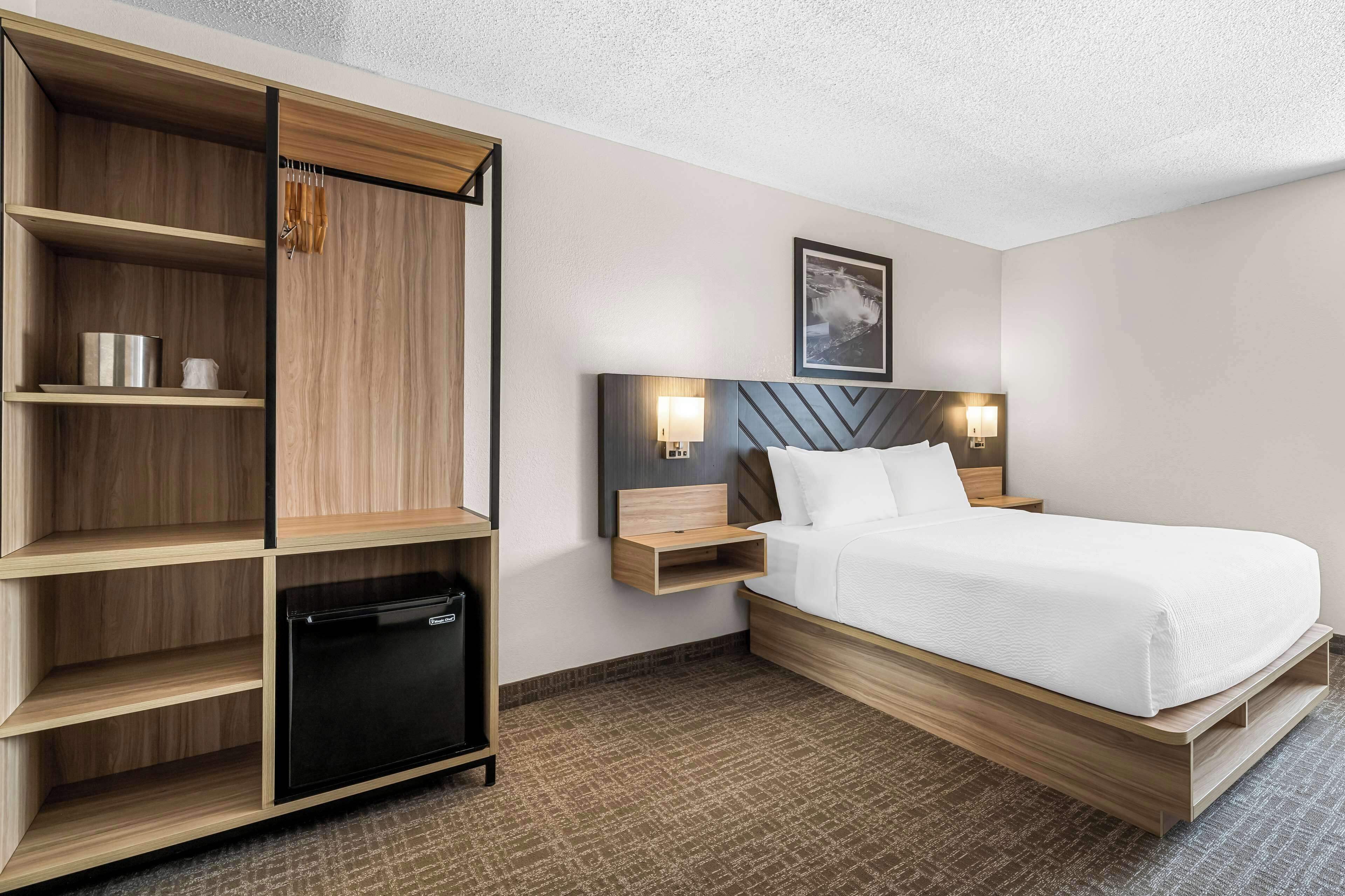 Habitación de hotel con cama, mesitas de noche, armario y mini nevera integrada.