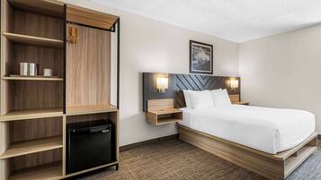 Habitación de hotel con cama, mesitas de noche, armario y mini nevera integrada.