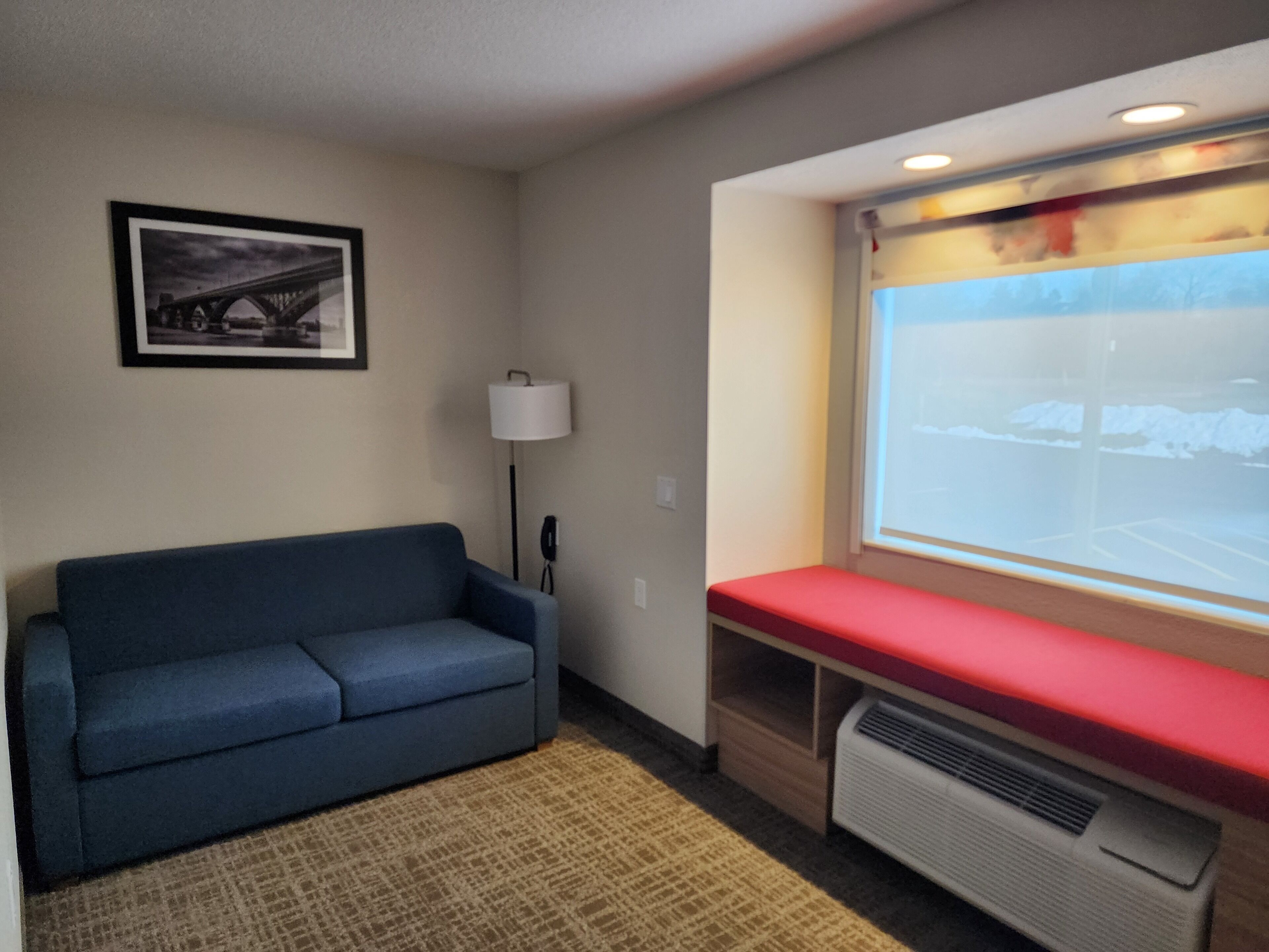 A room with a blue sofa, a red bench, a lamp, a heater, and a projector screen displaying a snowy landscape.