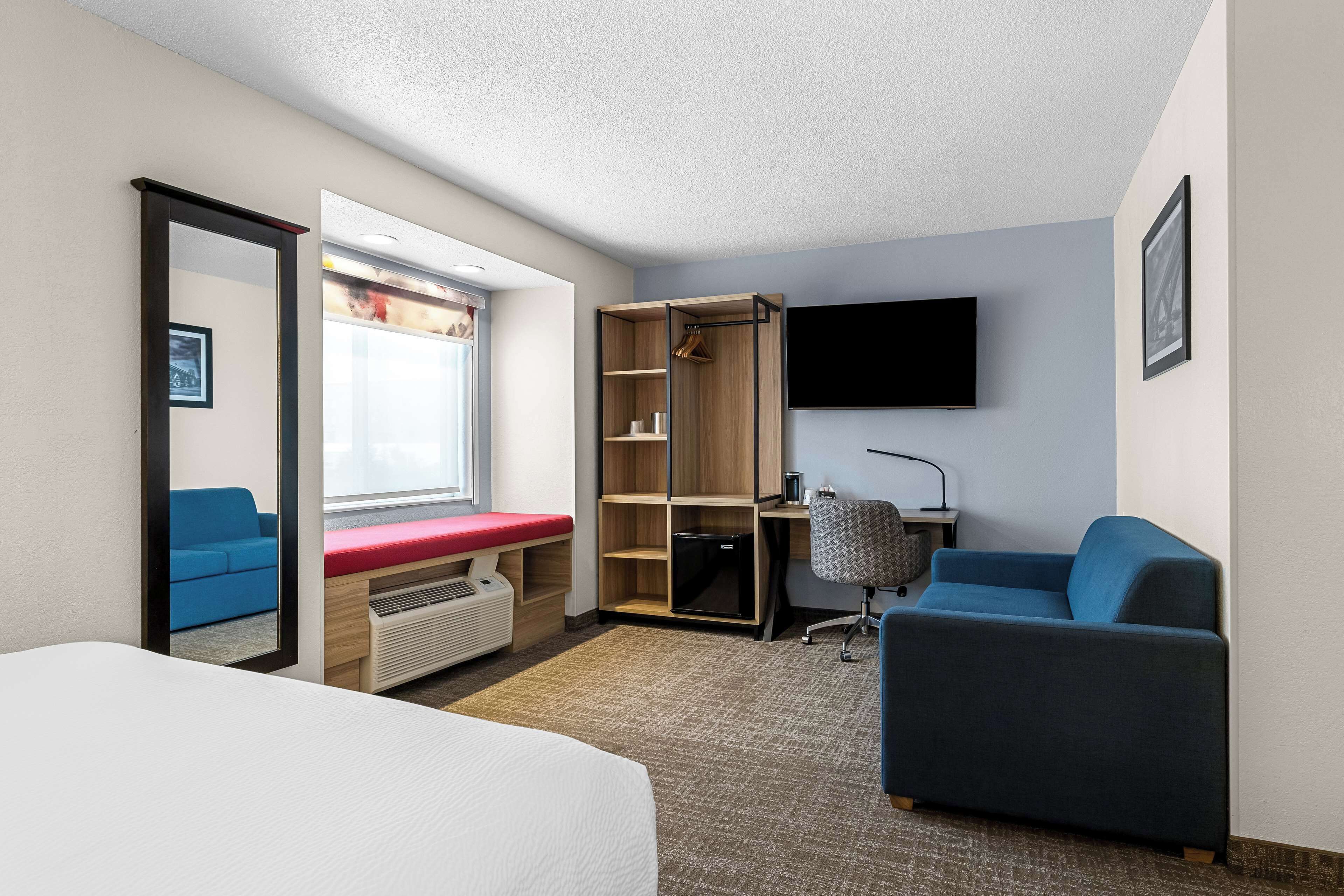 A hotel room with a bed, a desk, a chair, a wardrobe, a TV, and a window.