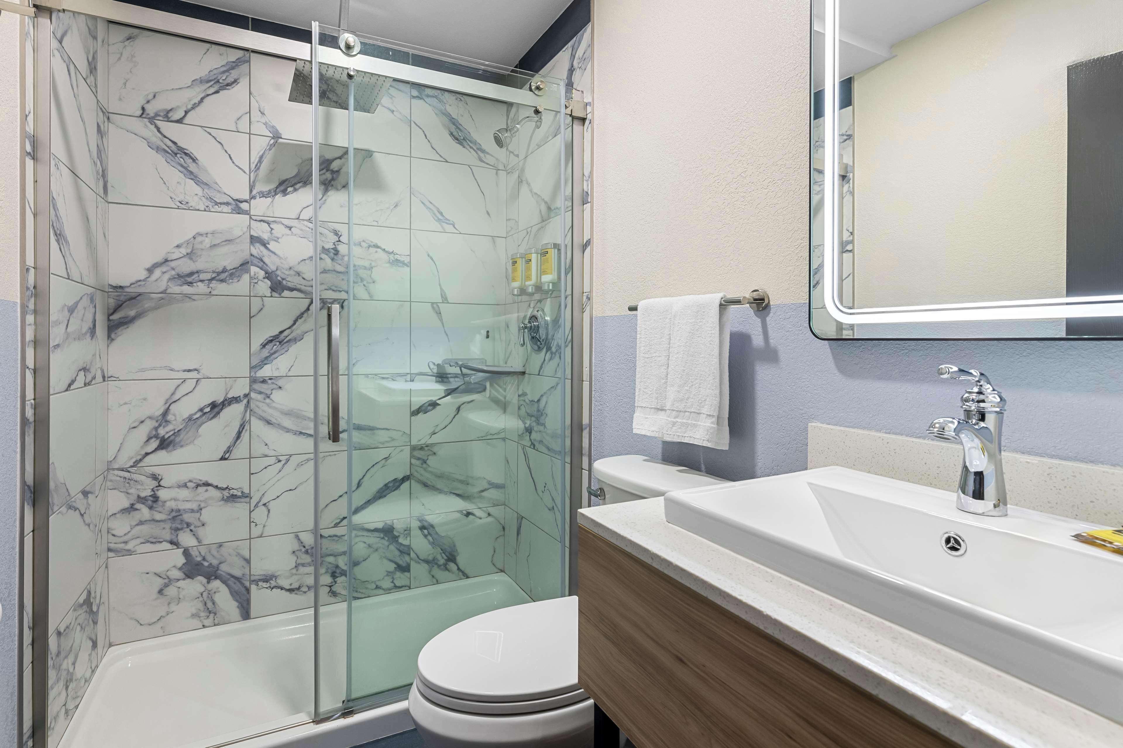 A bathroom with a glass-enclosed shower, a white toilet, a sink with a mirror, and toiletries on the wall.