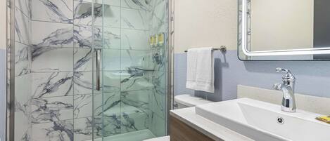 A bathroom with a glass-enclosed shower, a white toilet, a sink with a mirror, and toiletries on the wall.