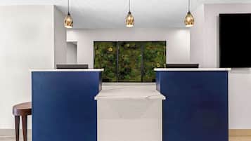 Un área de recepción de diseño moderno, con un amplio muro verde que presenta un mural inspirado en la naturaleza, un mostrador de recepción azul oscuro y tres lámparas colgantes.