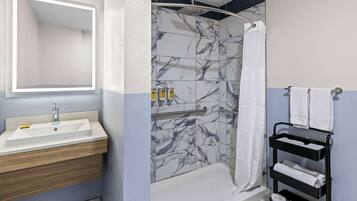 A bathroom with a sink, mirror, shower, and towel rack.