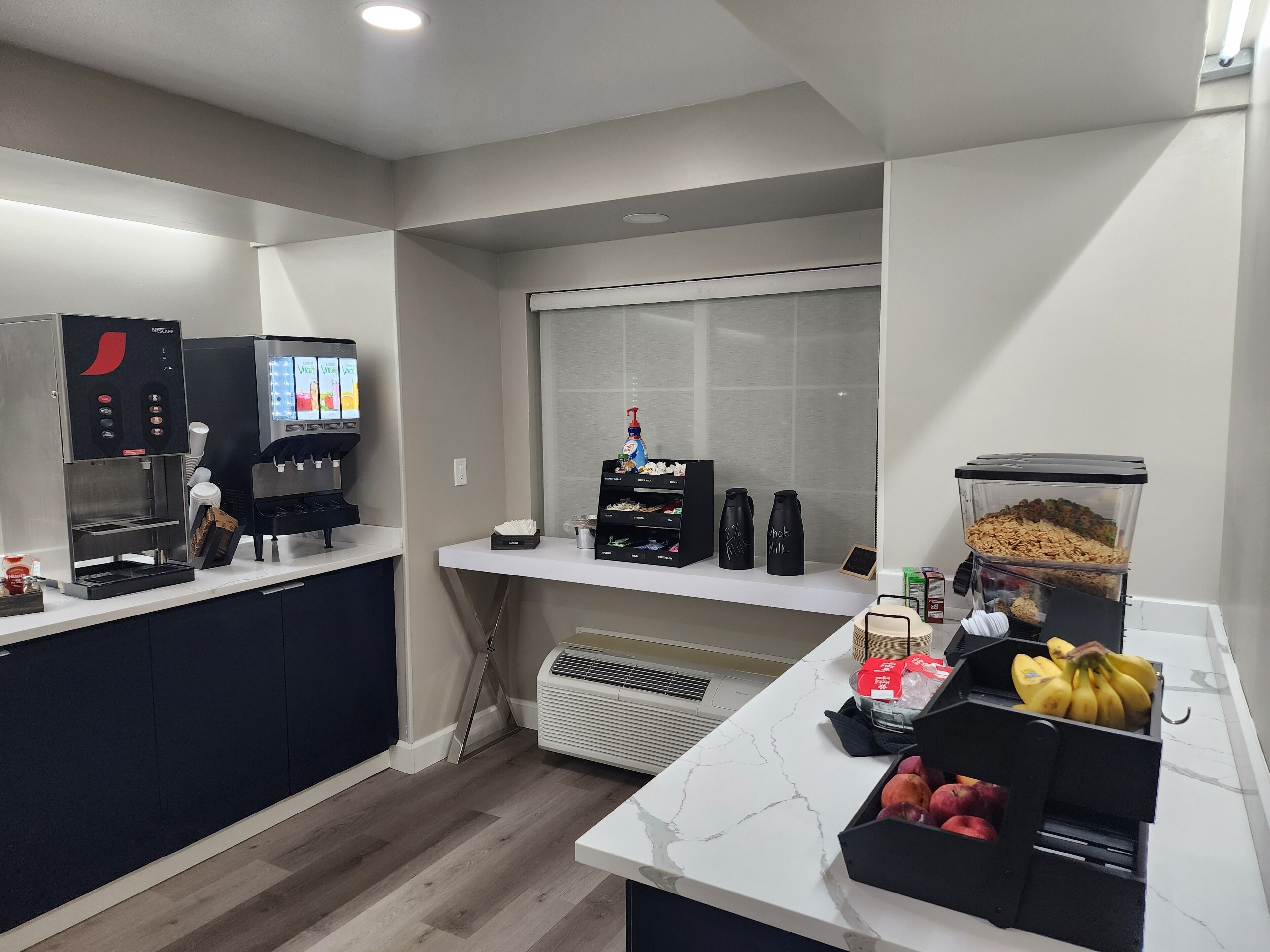 Una cocina moderna con una cafetera, una exposición de fruta y un ventanal con persianas.