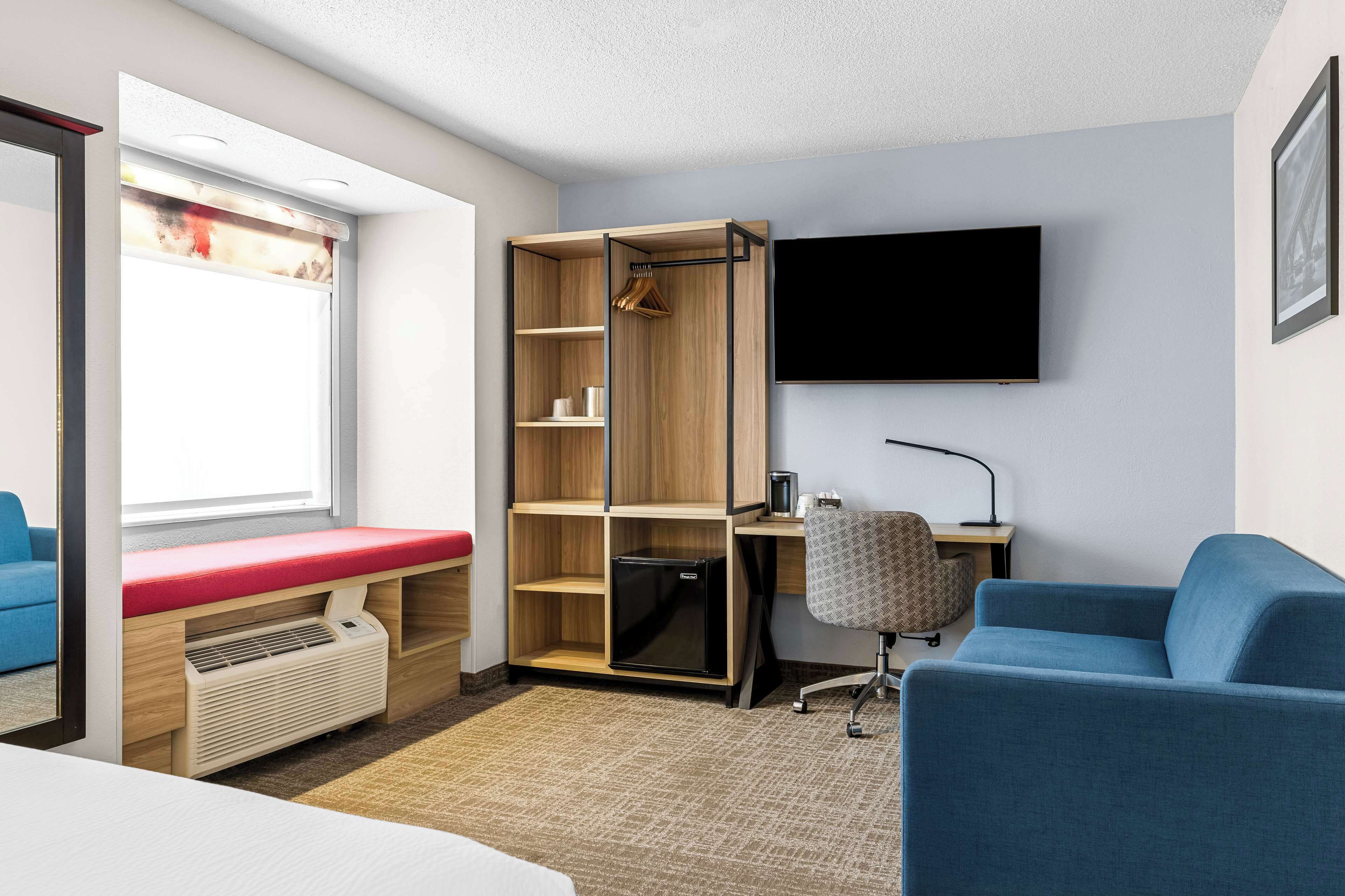 Ein kleines Hotelzimmer mit Bett, Schreibtisch, Stuhl, Fernseher und Kleiderschrank.