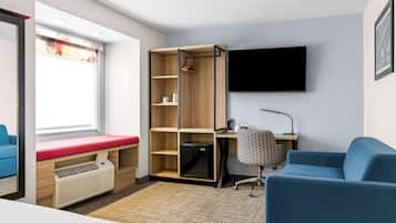Ein kleines Hotelzimmer mit Bett, Schreibtisch, Stuhl, Fernseher und Kleiderschrank.