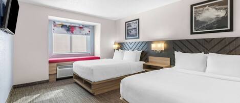 A hotel room with two beds, a window with a view, a mounted TV, and a framed picture on the wall.