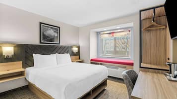 A hotel room with a large bed, bedside tables, a desk, a chair, a window with a view, and a mounted TV.