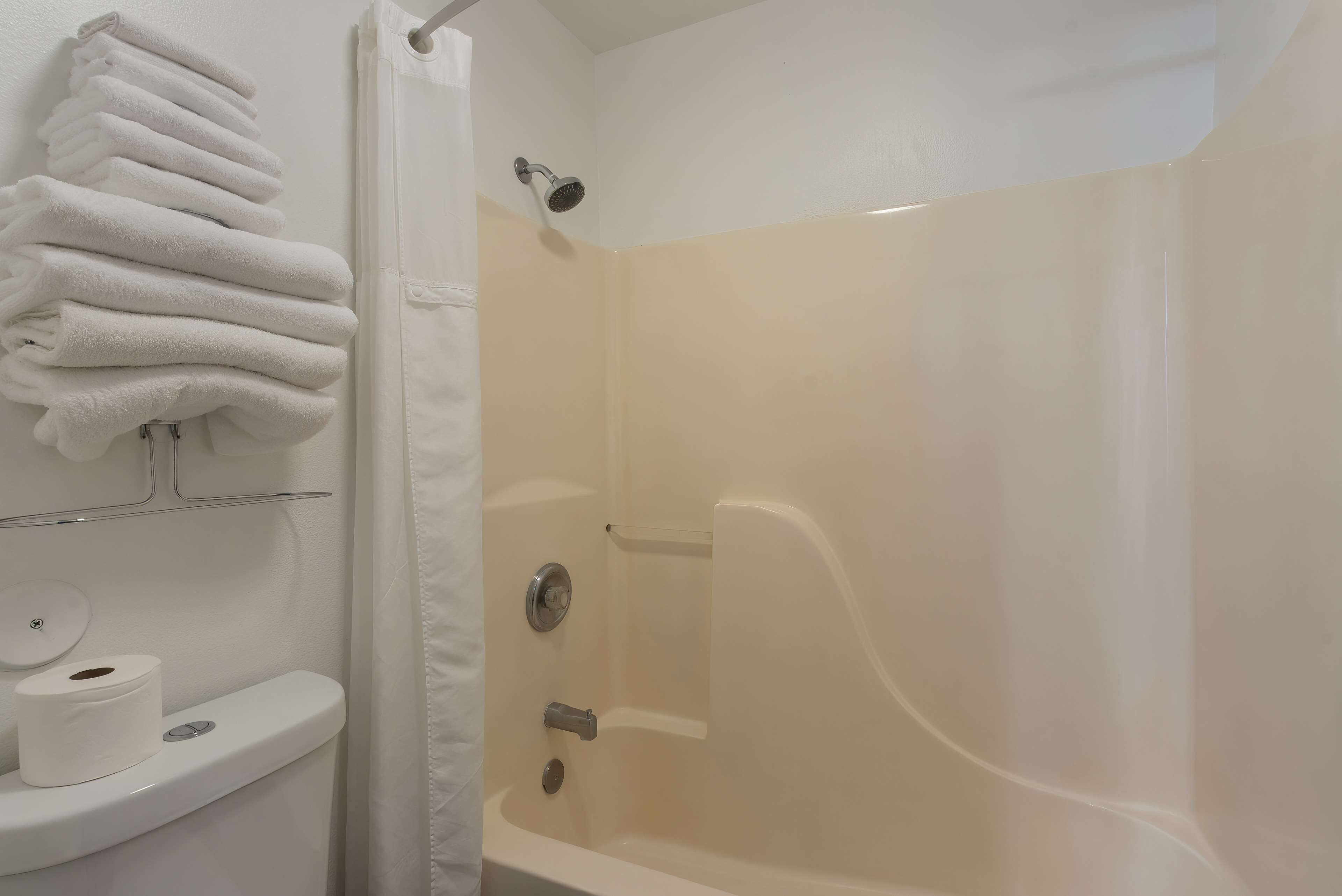 A bathroom with a toilet, a stack of white towels, and a shower area.