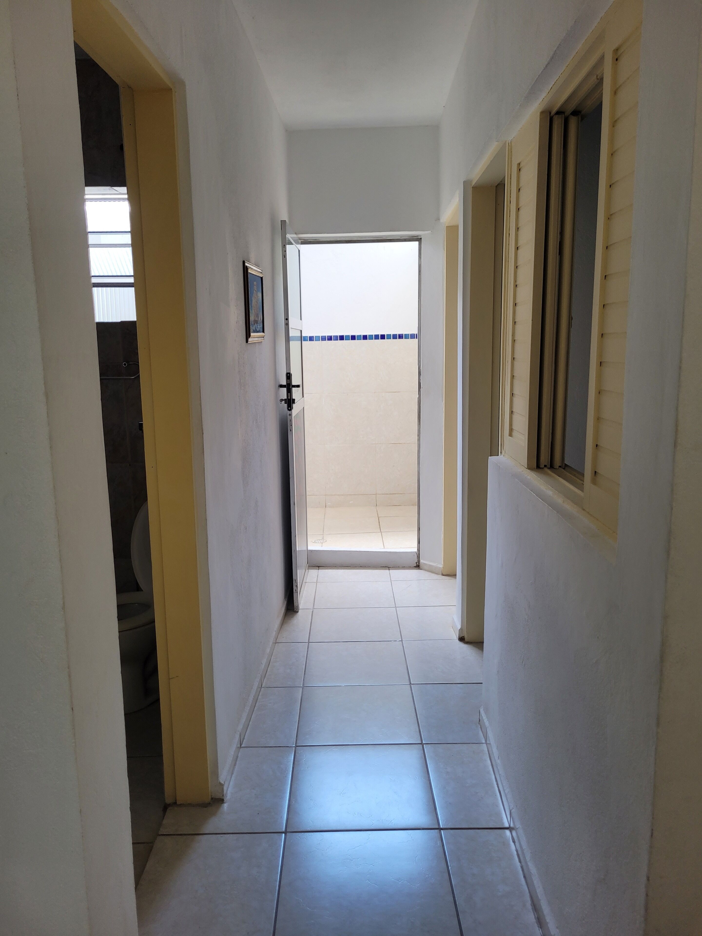 A hallway with white walls and tiled flooring leading to a door.