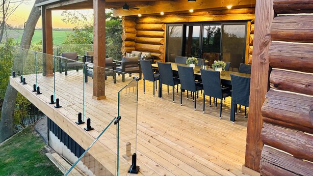 Een vakantiehuis in blokhutstijl met een houten terras, een zitgedeelte buiten en een grote schuifdeur naar een terras.