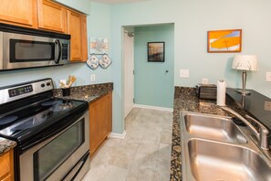 A kitchen with stainless steel appliances, granite countertops, wooden cabinets, and a view into the dining area.