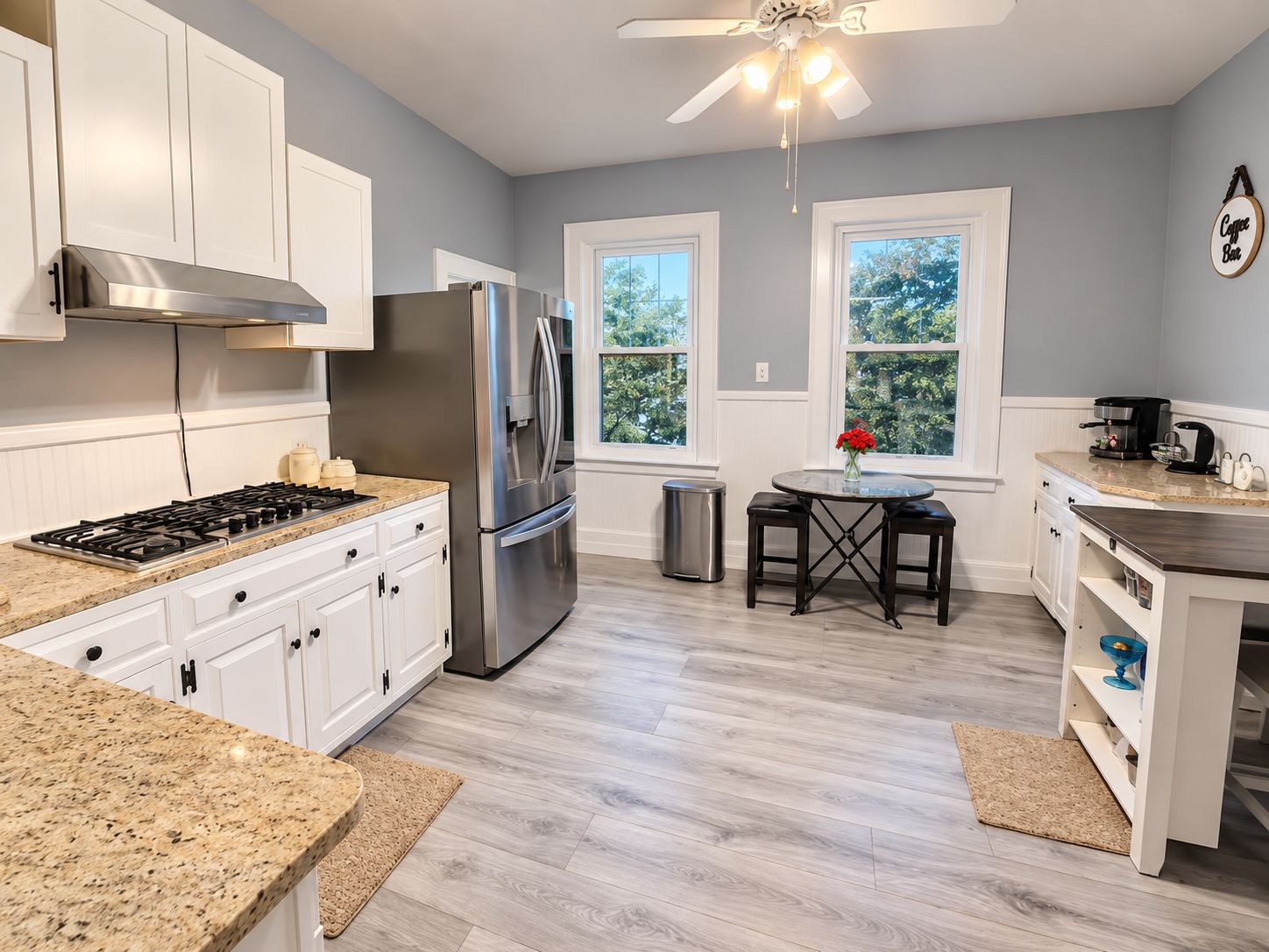 A modern kitchen with white cabinets, stainless steel appliances, a gas stove, and a ceiling fan.