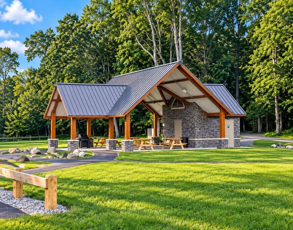 A rustic outdoor pavilion with picnic tables and a barbecue area, surrounded by a well-maintained lawn and trees. - Spacious Hidden Gem (Utica)