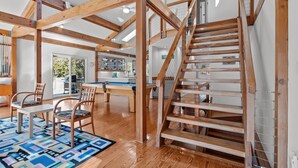 Une pièce spacieuse avec des poutres apparentes, une table de billard et un escalier.